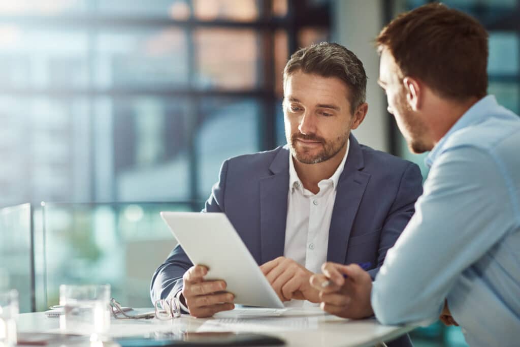 Teamwork meeting, tablet and business people in office workplace. Collaboration, technology and workers, men or employees with touchscreen planning sales, research or financial strategy in company SEO specialist explaining what on-page SEO is to his client while showing him examples on a tablet.